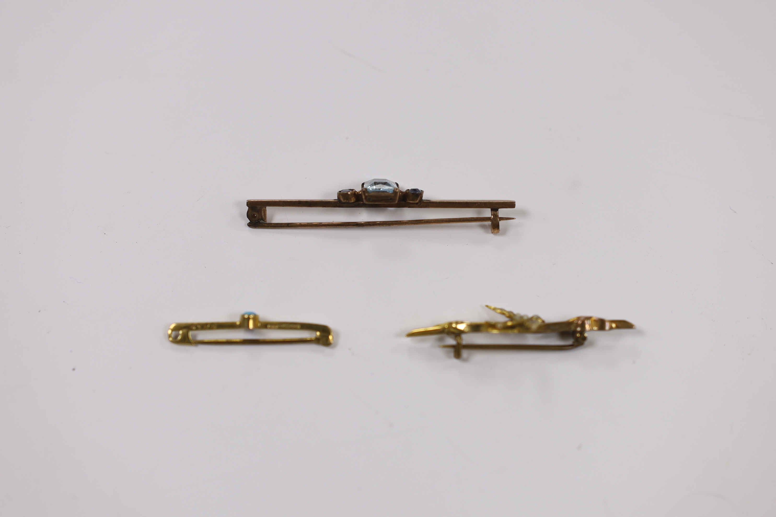 An Edwardian 9ct gold and seed pearl set swallow bar brooch, 43mm, a 9ct gold and turquoise set tie pin and a yellow metal, single stone aquamarine and two stone sapphire set bar brooch.